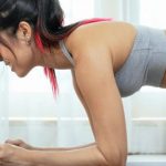 Home Workouts - Side view of sportive slim Asian female in activewear doing plank posture on mat near window with tulle in living room