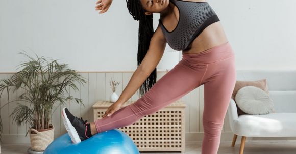 Home Workouts - Woman in Black Top and Pink Leggings Warming Up with Blue Fit Ball