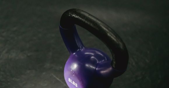Strength Training Tools - From above of single violet kettlebell with handle for weight training on black background