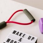 Strength Training Tips - From above composition of dumbbells and massage double ball and tape and tubular expanders surrounding light box with wake up and workout words placed on white surface of table