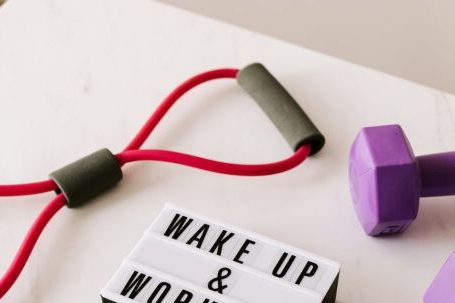 Strength Training Tips - From above composition of dumbbells and massage double ball and tape and tubular expanders surrounding light box with wake up and workout words placed on white surface of table