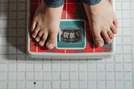 Weight Loss - From above crop anonymous barefoot child in jeans standing on weigh scales on tiled floor of bathroom