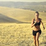 Cardio Fitness - Powerful young female athlete in activewear running along hill on background of mountainous landscape and listening to music in earphones during cardio training