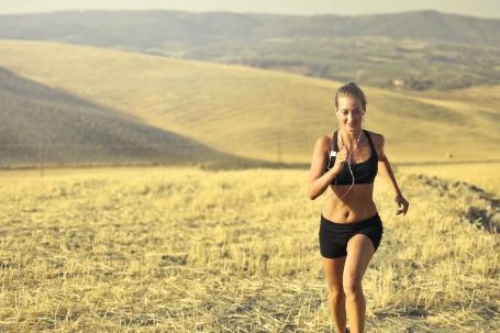Cardio Fitness - Powerful young female athlete in activewear running along hill on background of mountainous landscape and listening to music in earphones during cardio training