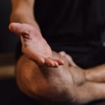 Mindful Practices - Crop unrecognizable barefoot male sitting with crossed legs on sports mat during stress relief meditation session