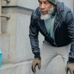 Lean Strength - Concentrated bearded senior black man wearing warm sportswear leaning forward with hands on knees and closed eyes in street near building while break in workout