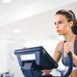 Weight Loss Maintenance - Serious fit woman in earphones and activewear listening to music and running on treadmill in light contemporary sports center
