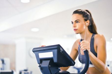 Weight Loss Maintenance - Serious fit woman in earphones and activewear listening to music and running on treadmill in light contemporary sports center