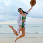 Long-term Success - Woman Jumping on Seashore and Holding Hat