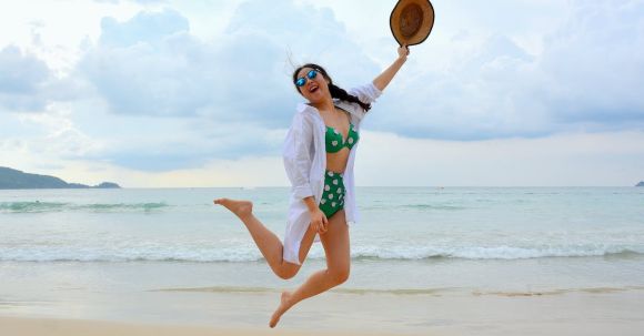Long-term Success - Woman Jumping on Seashore and Holding Hat