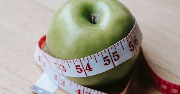 Fitness Nutrition - Green apple with measuring tape on table in kitchen
