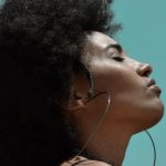 Fit On, Conquer - From below side view of young reflective ethnic female model with big earrings and closed eyes under blue sky