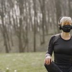 Meditation Challenge - Sportswoman in mask sitting in lotus pose in park