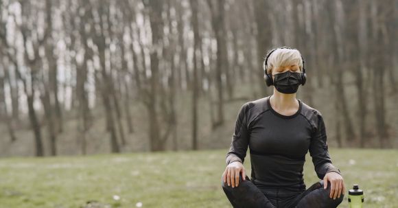 Meditation Challenge - Sportswoman in mask sitting in lotus pose in park