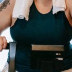 Fit Challenge - Smiling plus size female with towel exercising on cross trainer machine while looking at camera during workout in fitness studio