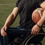 Sports Training - Man in Black Shirt and Blue Denim Jeans Sitting on Wheelchair Holding Basketball