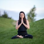 Yoga - woman in black tank top and black pants sitting on green grass field during daytime