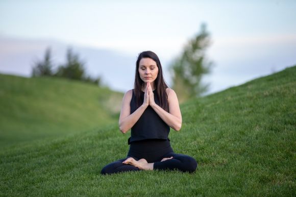 Yoga - woman in black tank top and black pants sitting on green grass field during daytime