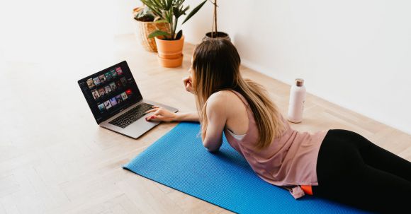 Online Fitness Training - Young woman lying on floor on mat while using laptop at home