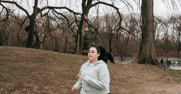 Order: Strength, Cardio - Full body motivated plus sized female in gray hoodie running in autumn park