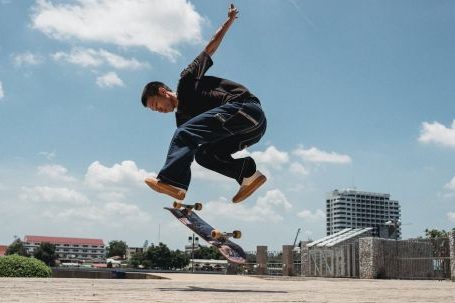 Next-level Training - Ethnic man jumping with skateboard on sidewalk