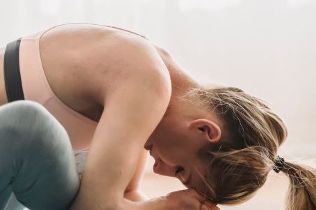 Mindful Fitness - Side view of focused young fit woman with long blond hair in sportswear stretching thighs while doing Baddha Konasana B yoga pose with closed eyes in sunny studio