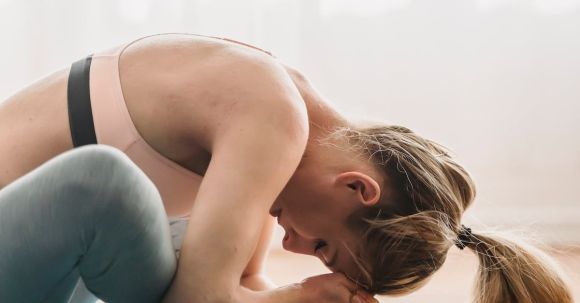 Mindful Fitness - Side view of focused young fit woman with long blond hair in sportswear stretching thighs while doing Baddha Konasana B yoga pose with closed eyes in sunny studio