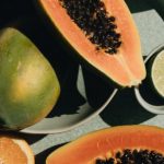 Portion Control - Top view of halves of ripe papaya together with oranges and limes placed on green round dishes and green fabric on white background