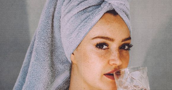 Body Transformation - Young woman with hair wrapped with towel and bared shoulders drinking water and looking at camera