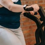 Weight Loss Programs - Side view of cheerful plus size ethnic female in activewear with towel exercising on fitness equipment during workout in gym