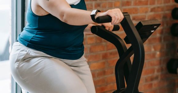 Weight Loss Programs - Side view of cheerful plus size ethnic female in activewear with towel exercising on fitness equipment during workout in gym