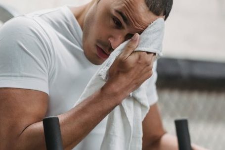 Pre-workout Fuel, Post-workout Recovery. - Young male wiping forehead with towel during rest after hard workout in contemporary fitness center